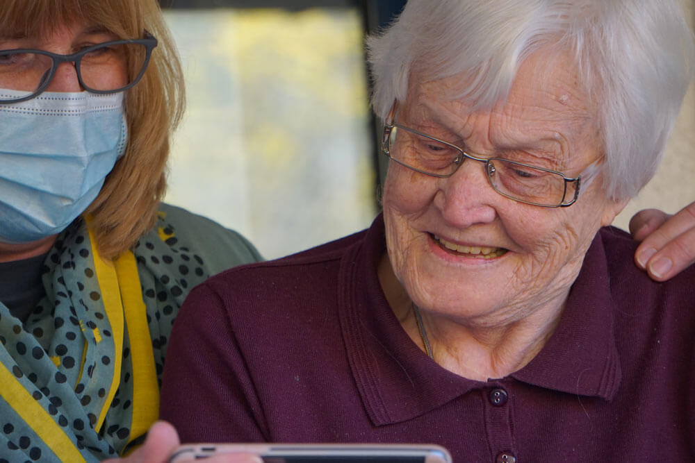 Elderly woman and daughter wearing a mask looking at a mobile device for ordering medicine online